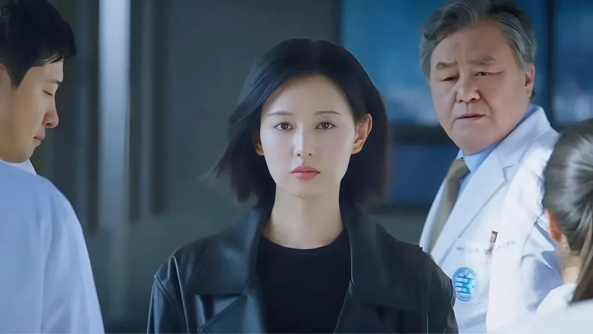 A woman in a black leather jacket stands among doctors in white coats while an older doctor watches her, in a still from Doctor X: Mafia in White