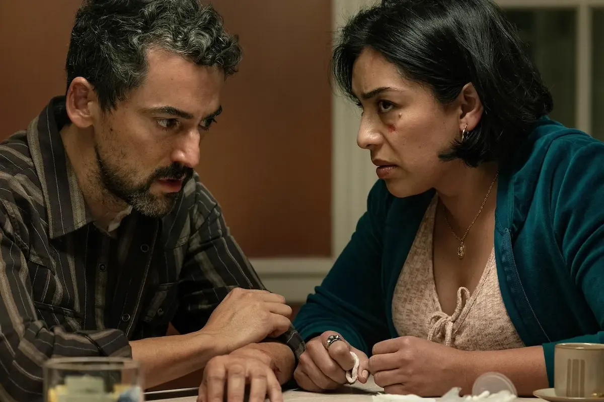 A man in a striped shirt and a woman with a cut on her cheek talk tensely across a table, in a still from Netflix’s Animals